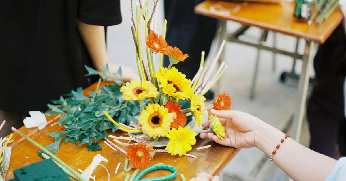 机の上で花を生ける独学用の本と、講師から学ぶフラワーアレンジメント教室の比較